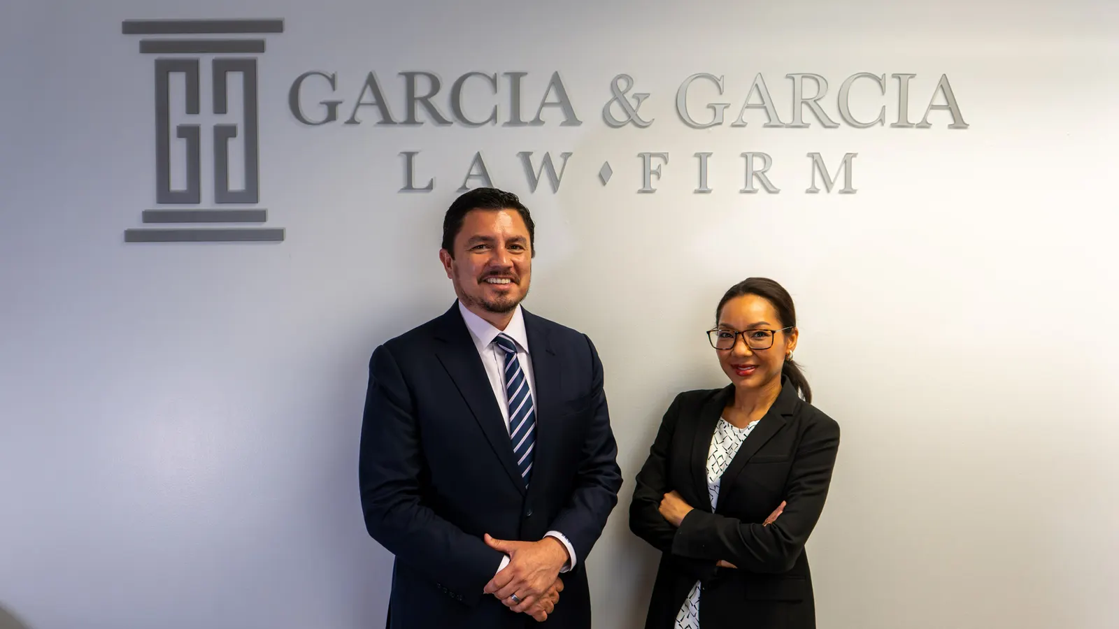 Two Garcia & Garcia attorneys in front of the firm's logo wall